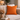 Harris Tweed Clementine orange cushion on a beige sofa with a cup, books, and decorative items in a cozy living room.