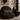 Black armchair with a Harris Tweed Dunmore Houndstooth lumbar cushion in a room with a vase of dried plants and a lamp.