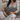 Person sitting on a couch holding a Harris Tweed Grey Herringbone lumbar cushion wearing a gray sweater and pants.