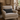 Beige armchair with a Harris Tweed Charcoal Herringbone lumbar cushion in a cozy room with stone walls and a window.