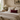 Neatly made bed with a Harris Tweed Claret red lumbar cushion in a bedroom with floral wallpaper.