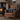 Brown leather armchair with a Harris Tweed Denim MacLeod cushion  in front of a fireplace.