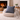 Harris Tweed Lomond Barleycorn cushion  on a beige ottoman in front of a fireplace