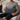 Man holding a Harris Tweed Lomond Barleycorn lumbar cushion on a couch in a cozy living room setting