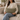 Woman holding a Harris Tweed Lovat Herringbone lumbar cushion on a couch in a cozy living room.