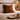 Cozy bedroom scene with Harris Tweed Moss, Gingerbread & Wine cushion, book, mug, and glasses on a tray.