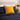 Mustard yellow Harris Tweed cushion on a bed with a vase of yellow tulips on a nightstand.