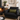 Cozy living room with a black armchair, fireplace, and Harris Tweed Olive lumbar cushion.