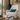 White rocking chair with a Harris Tweed Peacock lumbar cushion in front of a stone fireplace.