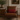 Brown leather armchair with a red Harris Tweed Royal Stewart Tartan lumbar cushion in a room with a wooden side table and framed painting.