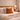 Neatly made bed with Harris Tweed Terracotta cushion and a lamp on a nightstand in a bedroom.