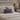 Neatly made bed with Harris Tweed Thistle & Flint Wave lumbar cushion and nightstand with lamp and books in a bedroom setting.