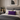 Neatly made bed with gray and beige bedding, Harris Tweed Thistle lumbar cushion, and nightstand with decor items.