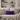 Beige sofa with a Harris Tweed Thistle lumbar cushion and decorative items on shelves in the background